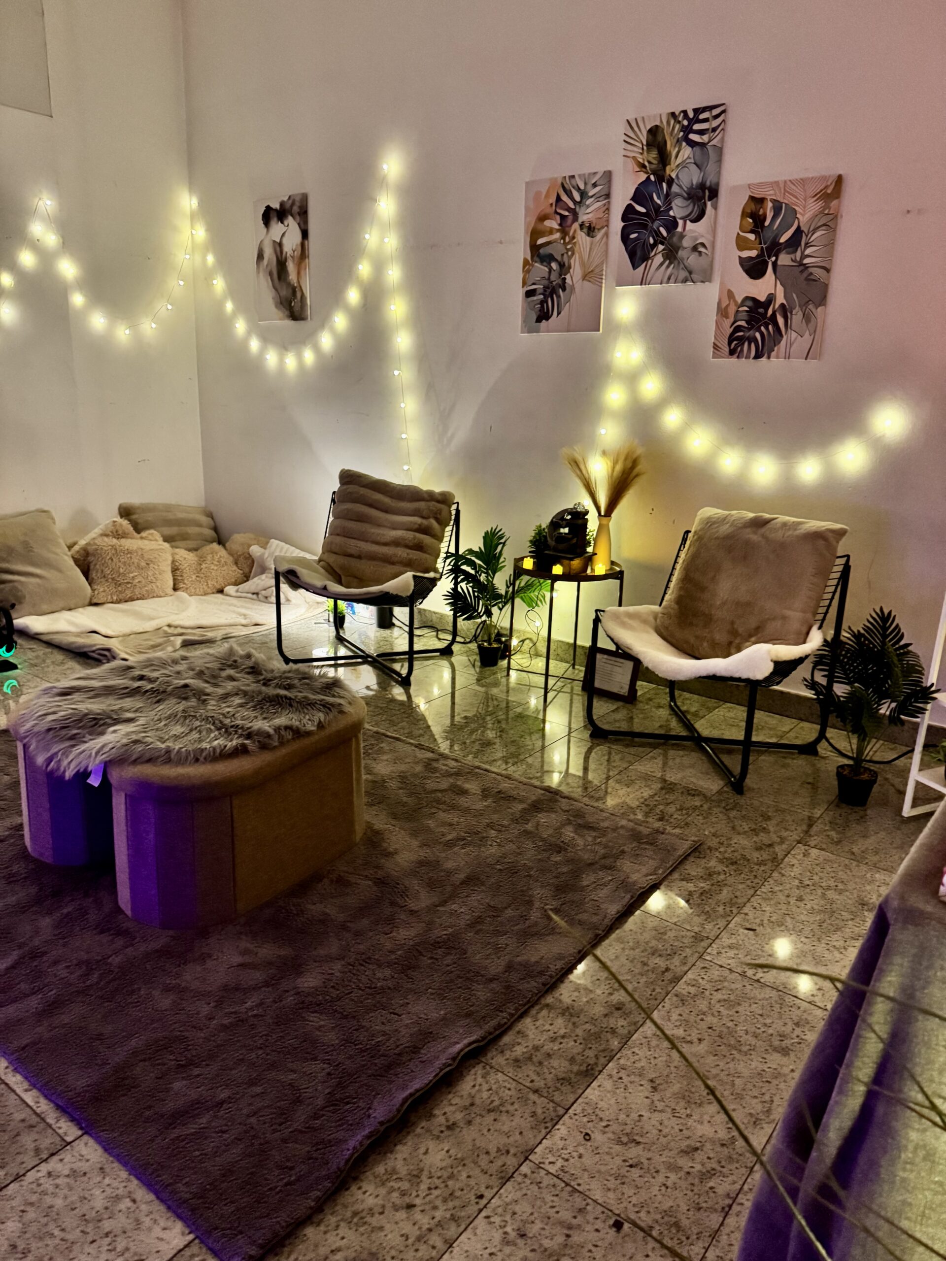 Fake fur ottomans, curved chairs, monstera art, pampas, and plants under fairy lights