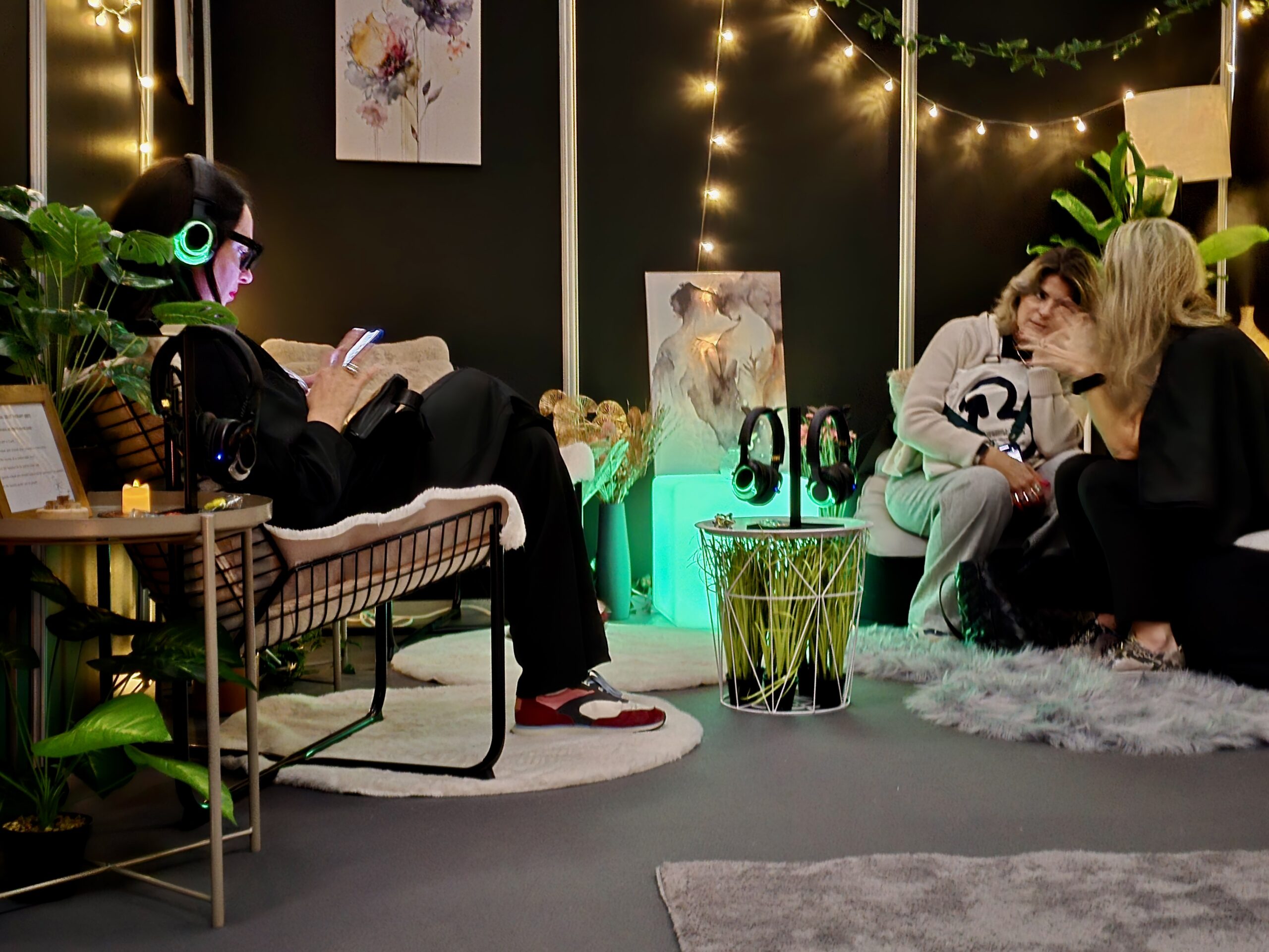 Diverse group relaxing in Calm Nest sensory lounge at event with headphones soft seating plants fairy lights.