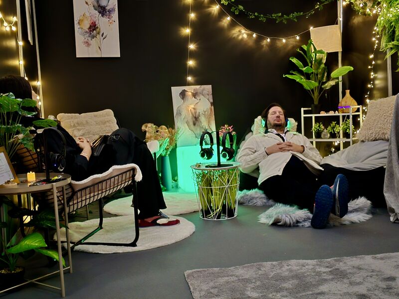 Diverse group relaxing in Calm Nest sensory lounge at event with headphones soft seating plants fairy lights