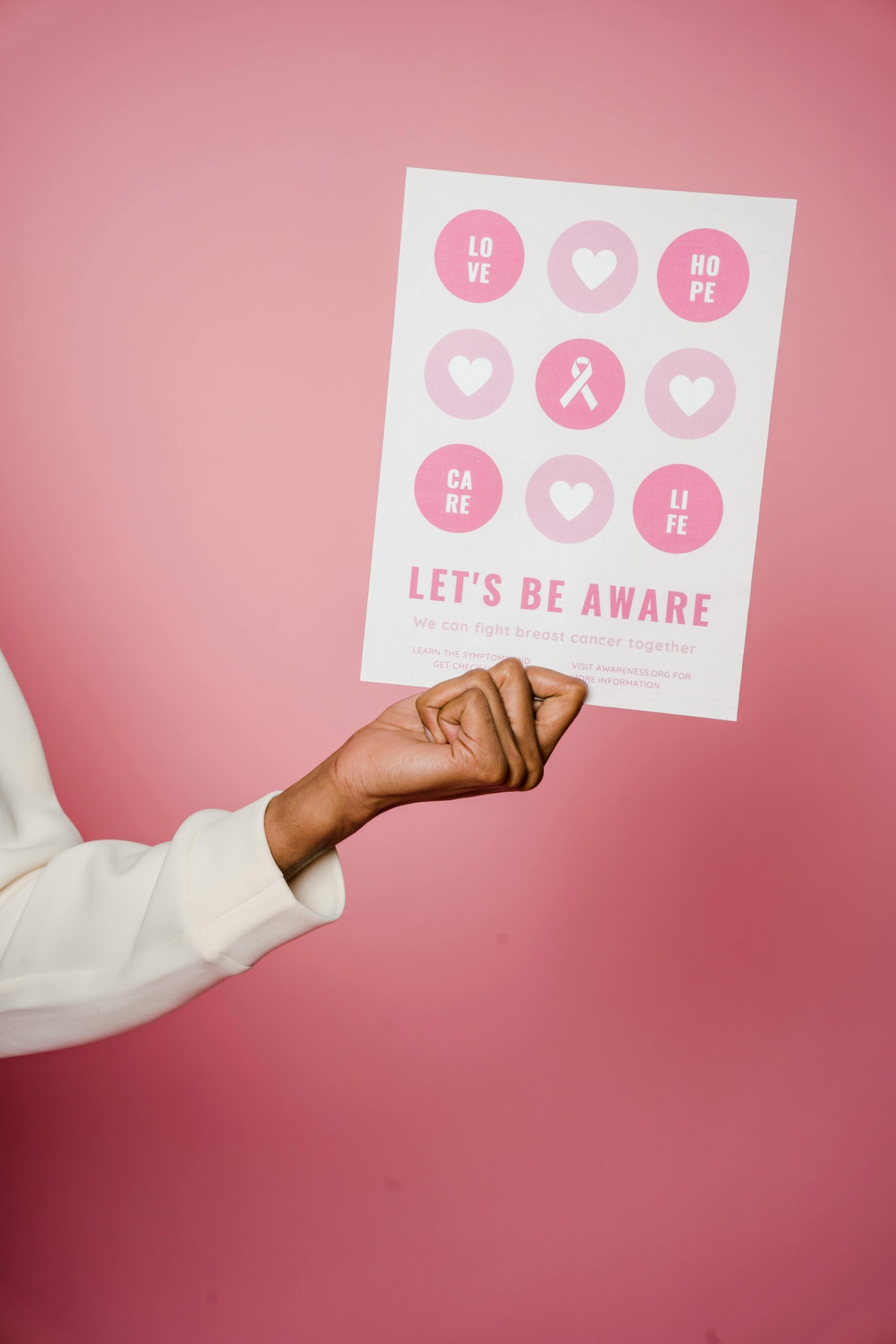 A person holding a pink awareness campaign poster with the words 'Let's Be Aware', representing inclusive wellbeing campaigns and advocacy at events